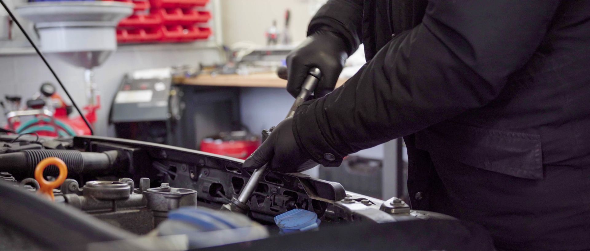 Eine Person mit schwarzen Handschuhen beschäftigt sich mit dem Motor eines Fahrzeugs.